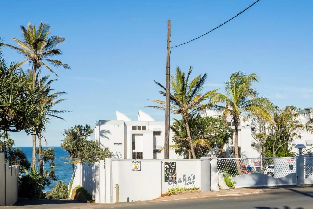 White beachfront apartment building with palm trees seen from the street at Chaka's Cove, Ballito