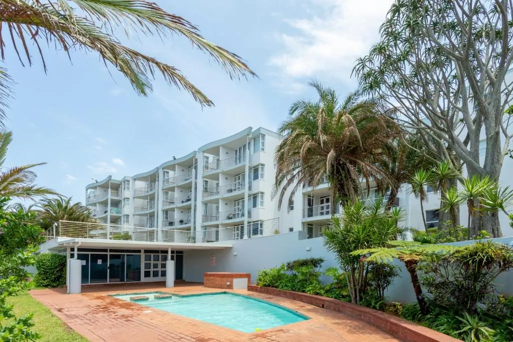 Pool on site with palm trees and the apartment building behind at Chaka's Cove, Ballito
