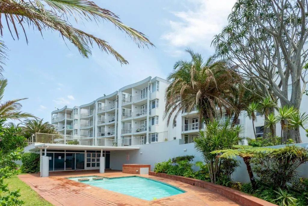 Pool on site surrounded by palm trees with the apartment building behind at Chaka's Cove, Ballito